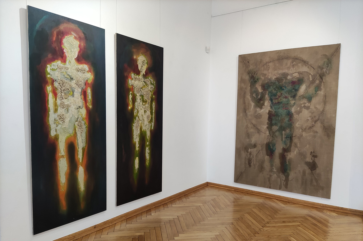 Widok wystawy z trzema obrazami przedstawiającymi ludzkie sylwetki