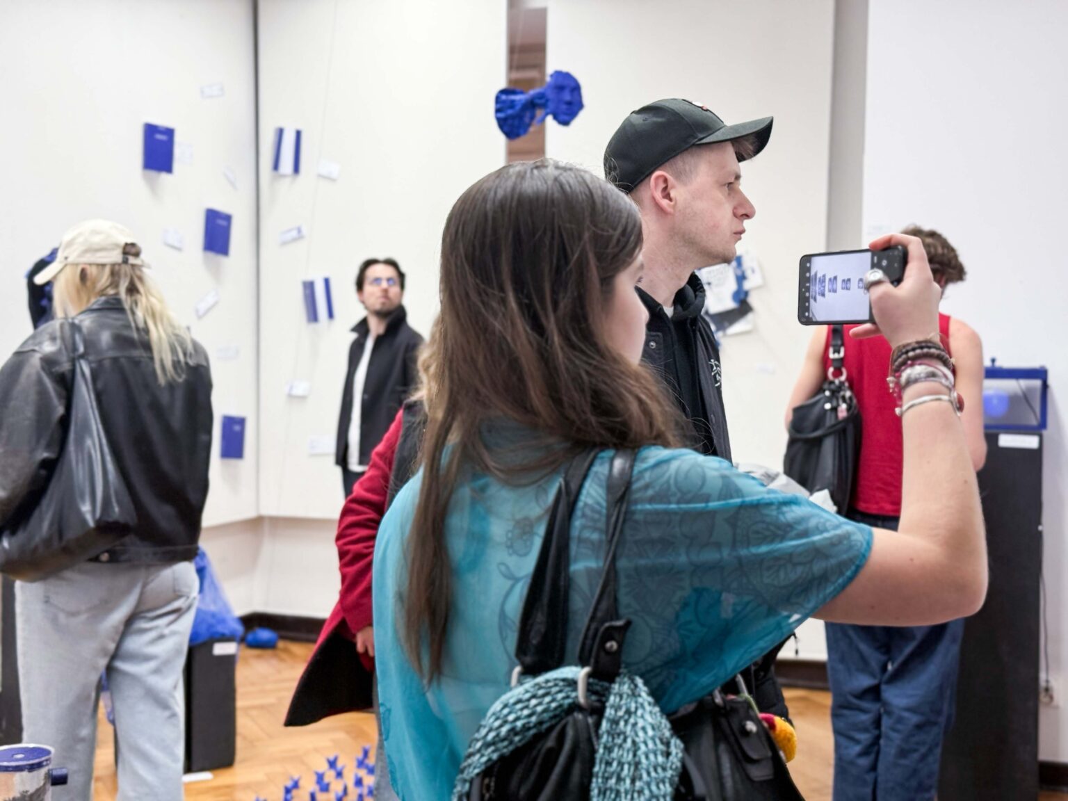 Dwie osoby na pierwszym planie, robią zdjęcia wystawy
