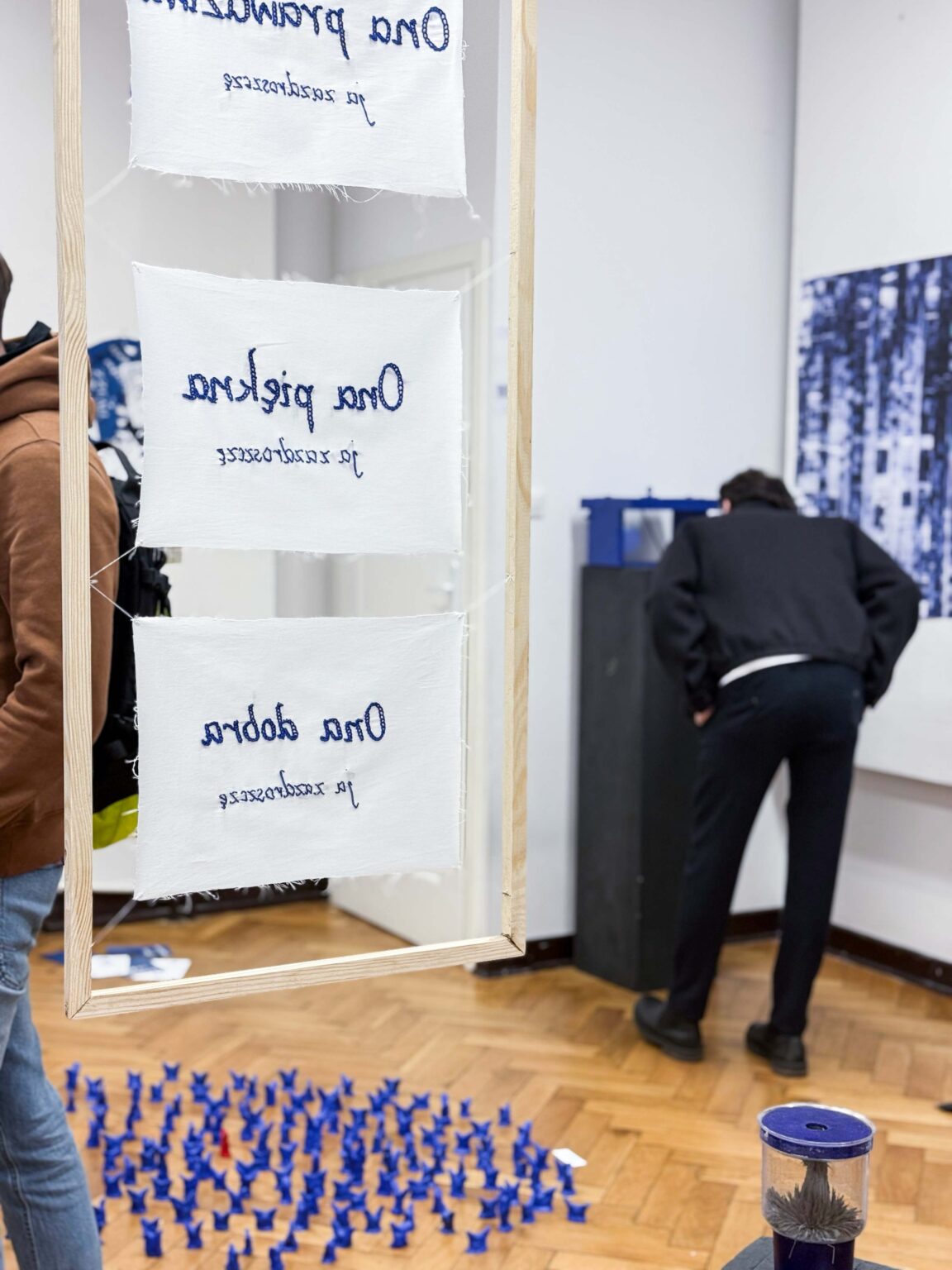 Praca wyszywana ręcznie ultramarynową nitką na białym tle w ramkach, z napisami: Ona piękna, Ona dobra, Ona prawdziwa