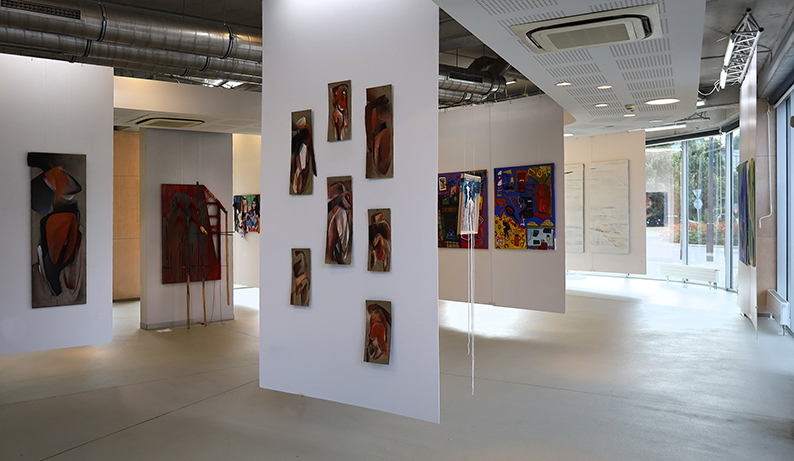 Widok prac wiszących w przestrzeni na słupie pośrodku, okna po prawej stronie zdjęcia