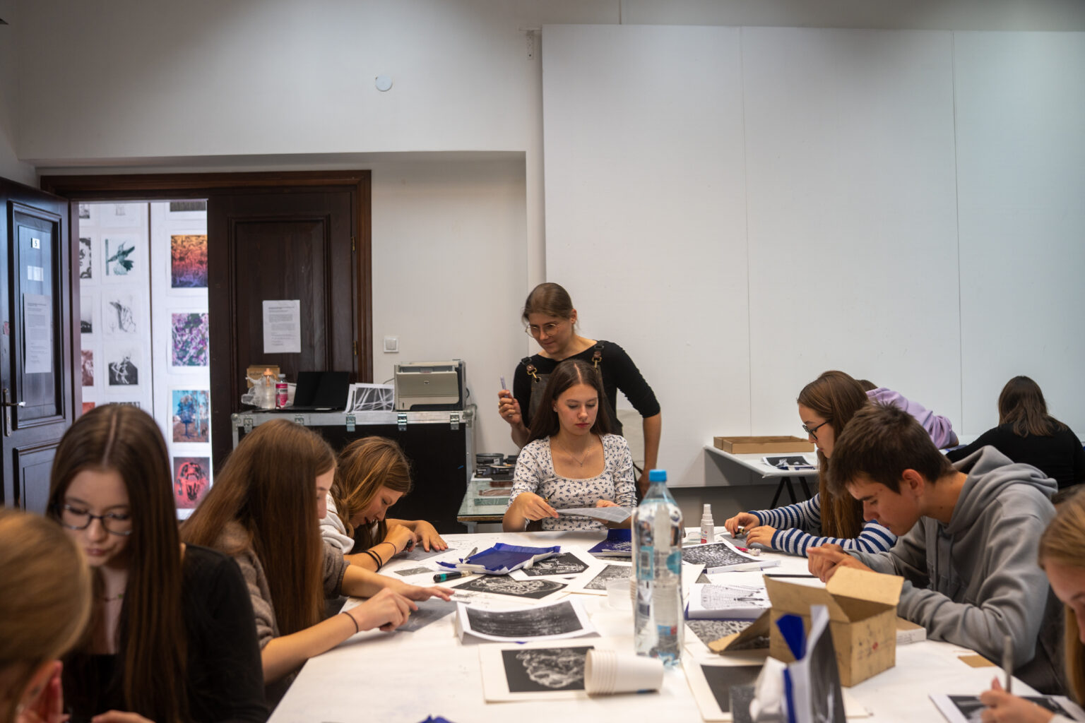 Grupa uczniów przy stole, wycinająca linoryty podczas warsztatów