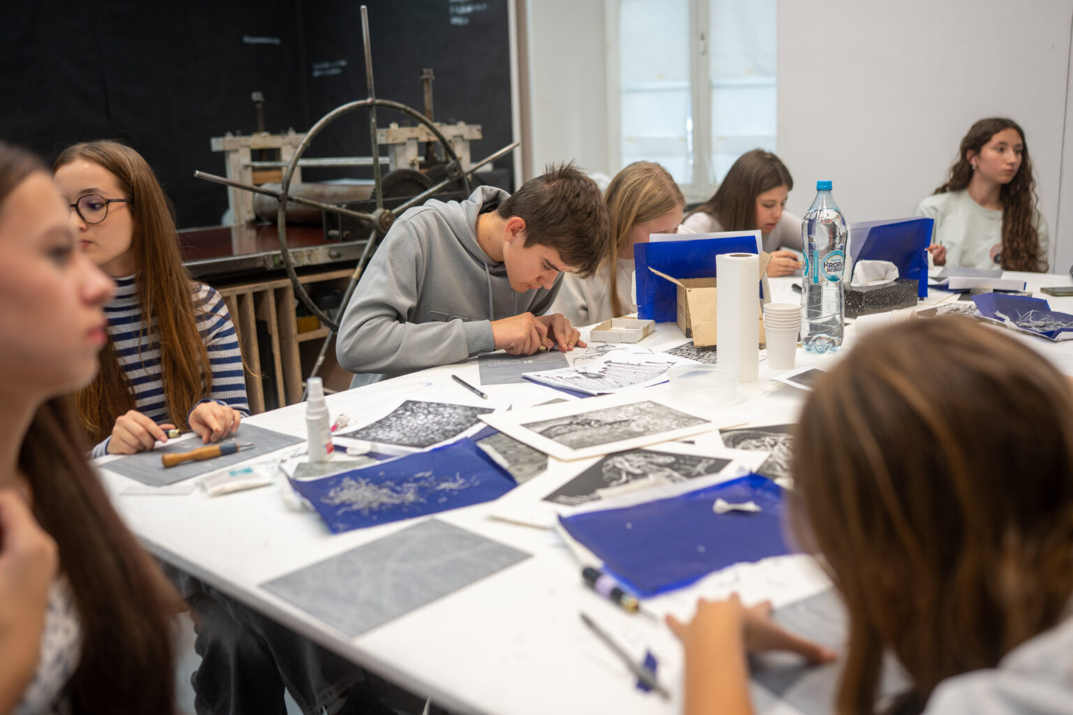 Grupa uczniów przy stole, wycinająca linoryty podczas warsztatów