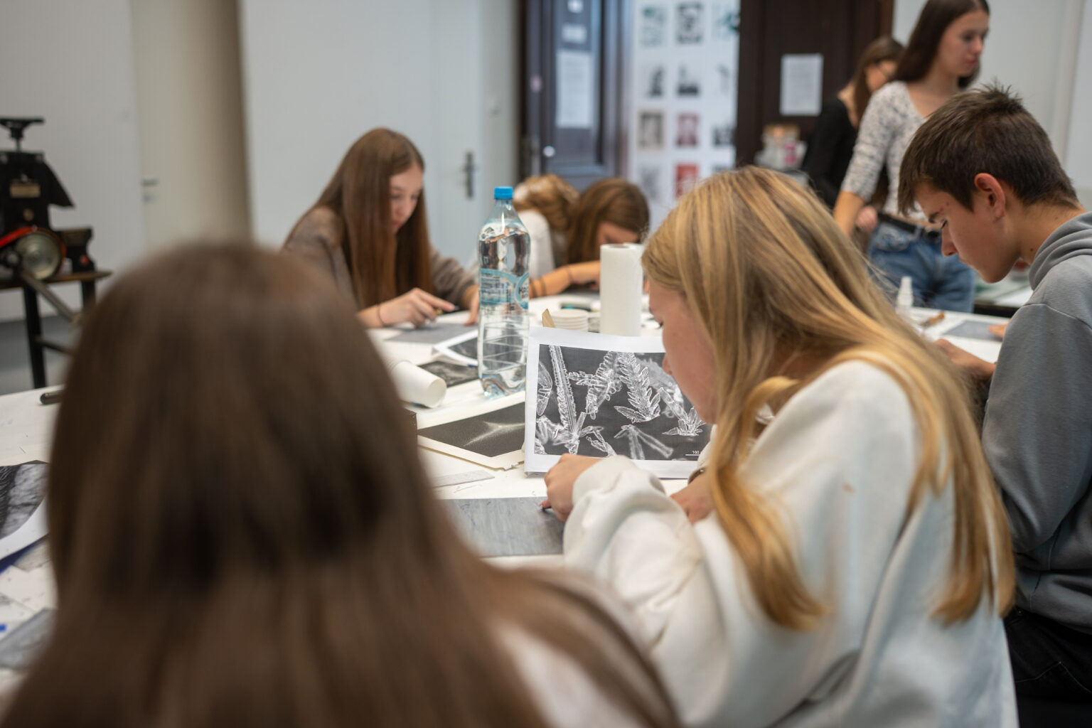 Grupa uczniów przy stole, wycinająca linoryty podczas warsztatów