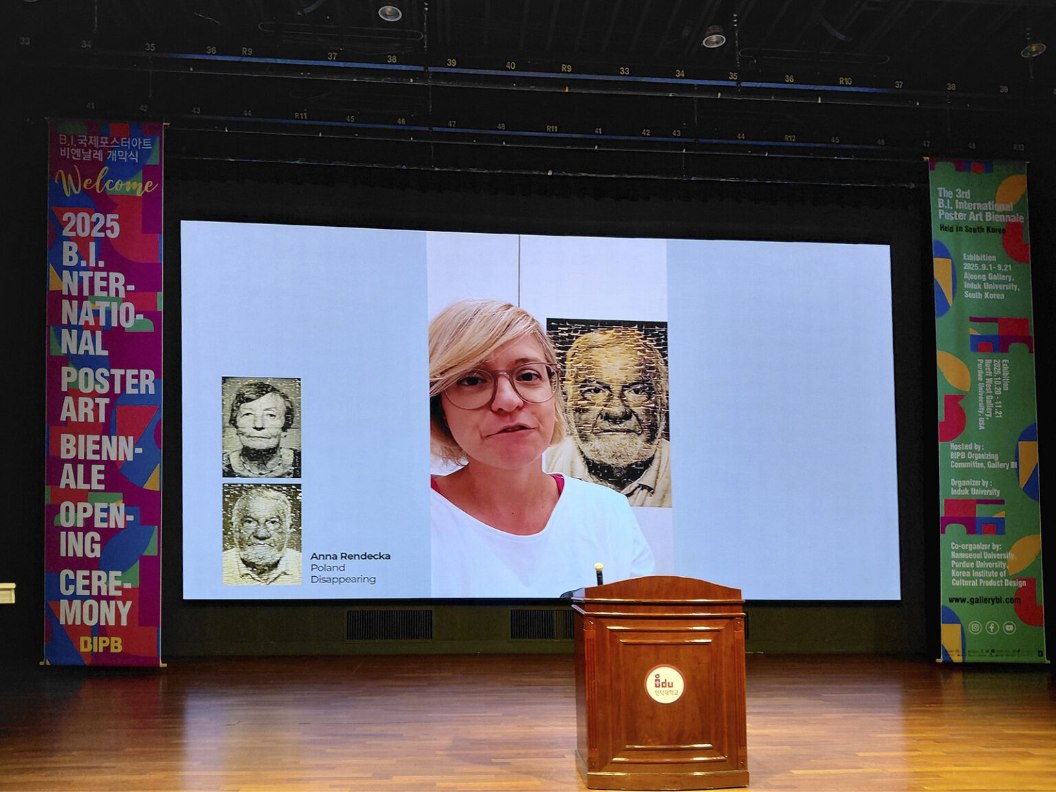 Praca Anny Rendeckiej wyświetlana na ekranie za sceną z podium.