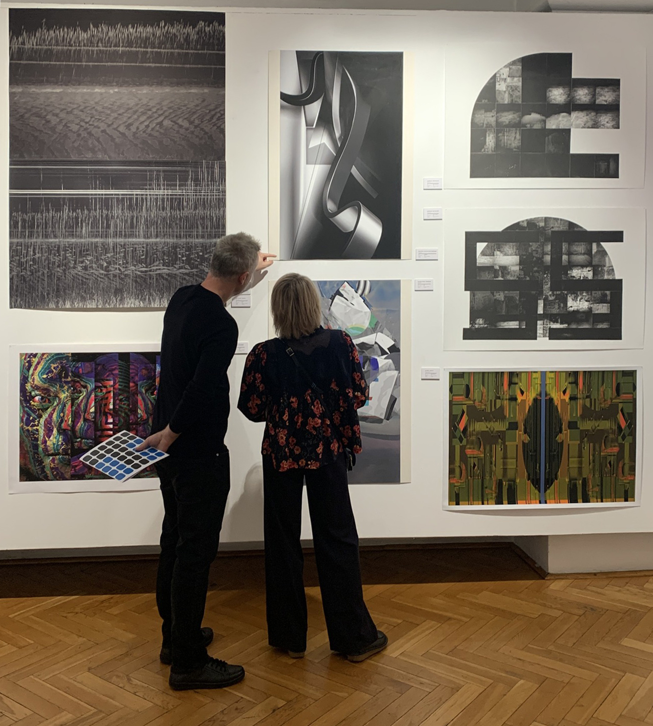 Dwoje zwiedzających ogląda wiszące na ścianie grafiki.