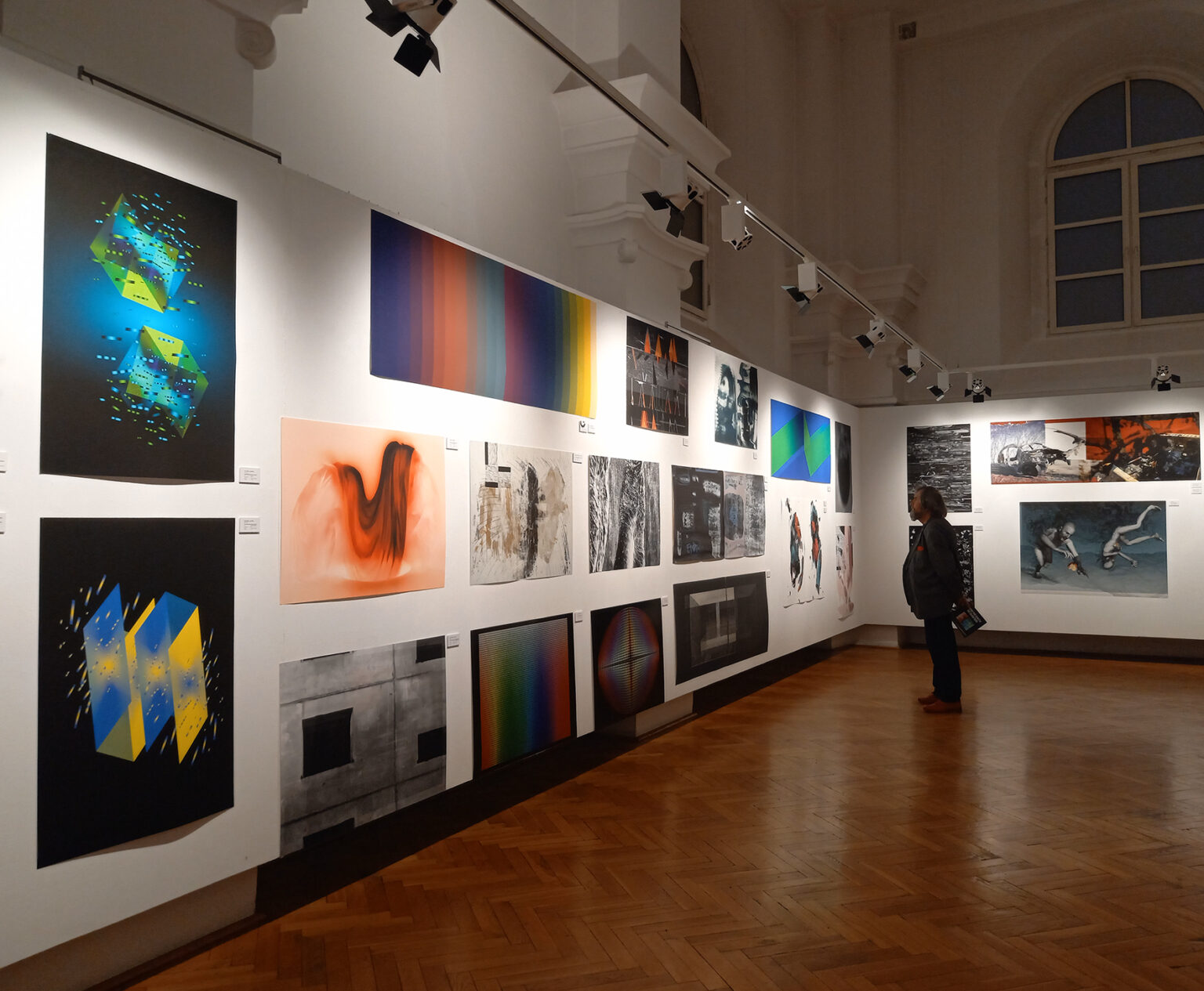 Widok prac graficznych wiszących na ścianie od lewej do prawej, mężczyzna oglądający grafiki.