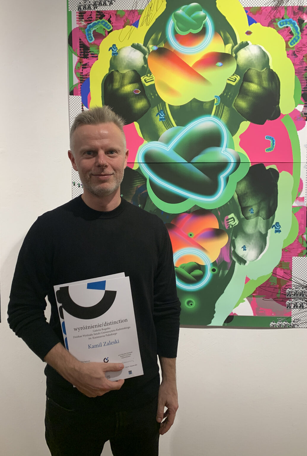 Artysta Kamil Zaleski przy swojej pracy graficznej z wyróżnieniem.