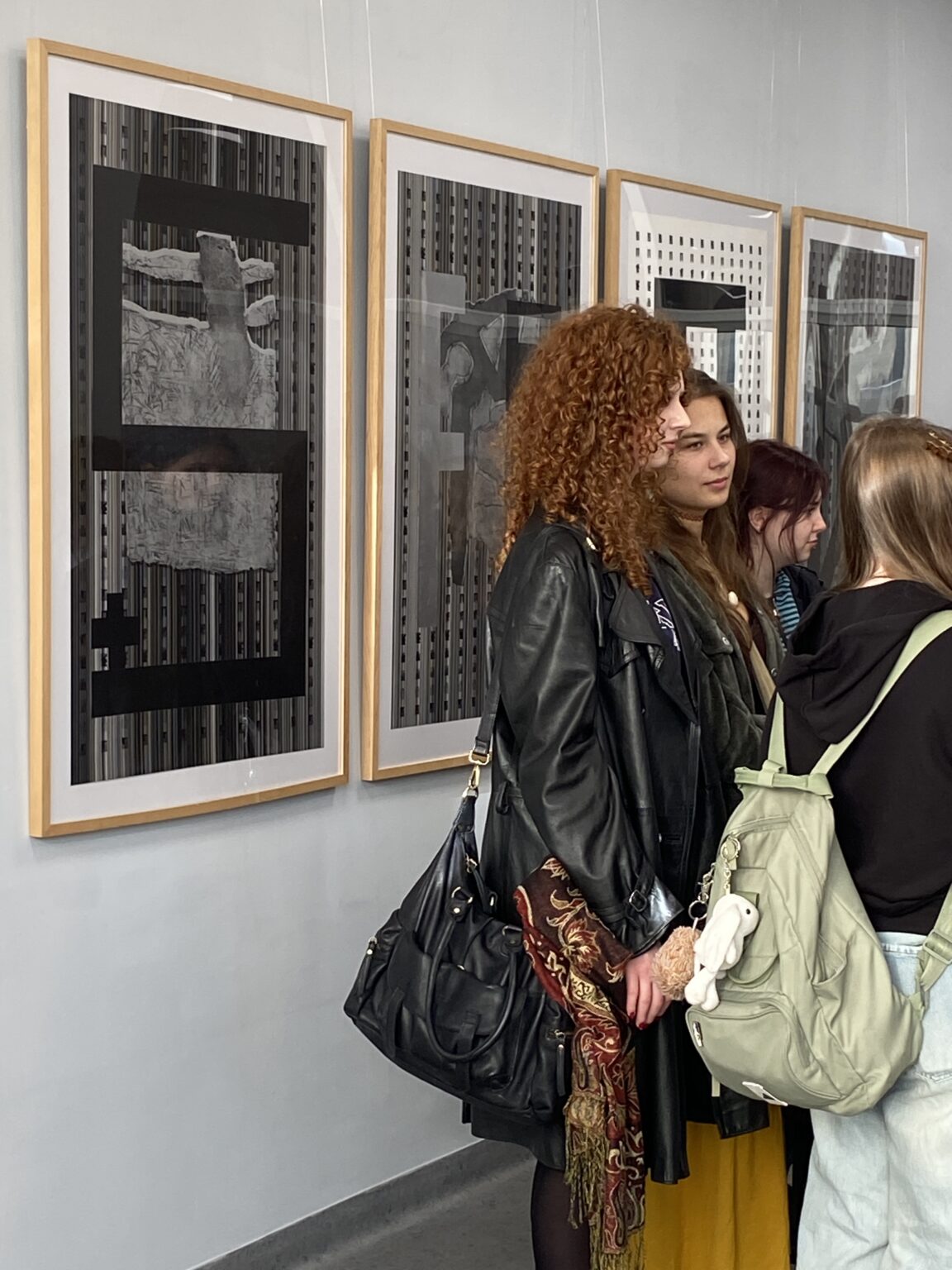 Widok otwarcia wystawy prac graficznych z osobami zwiedzającymi w sali.