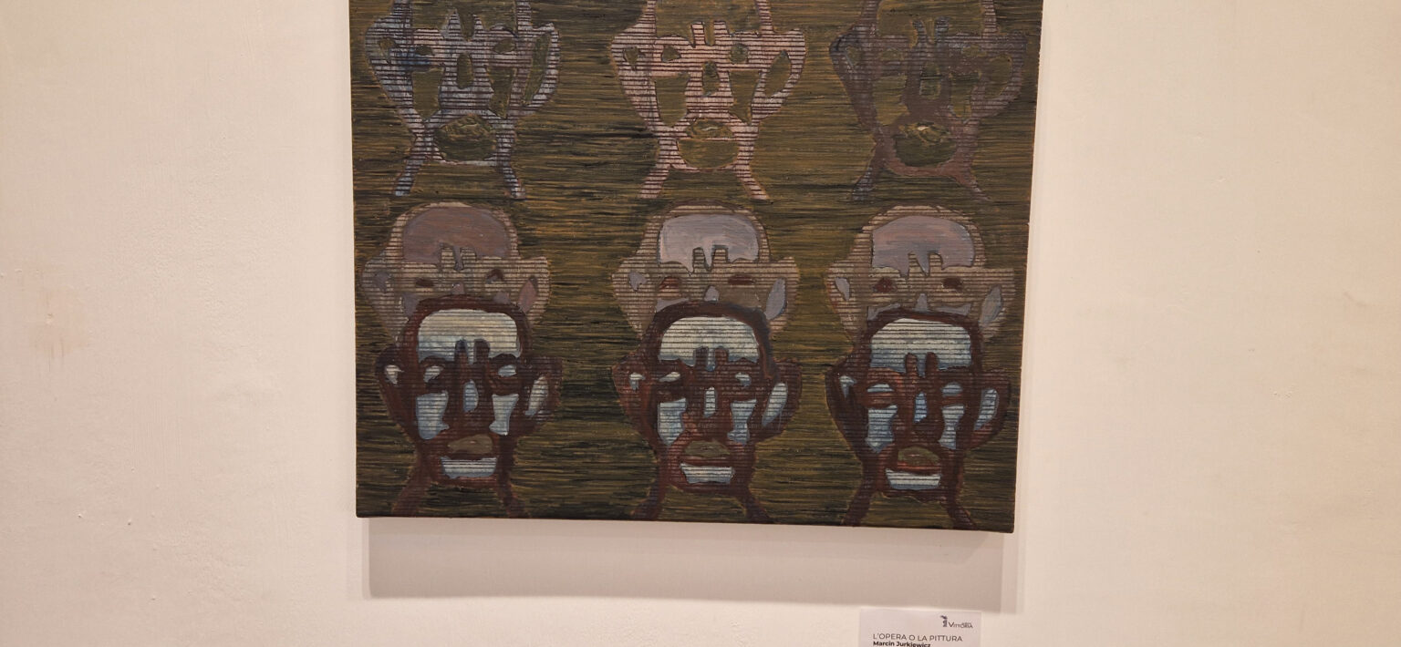 Widok obrazu Marcina Jurkiewicza ze zmultiplikowanymi twarzami na białej ścianie w galerii.