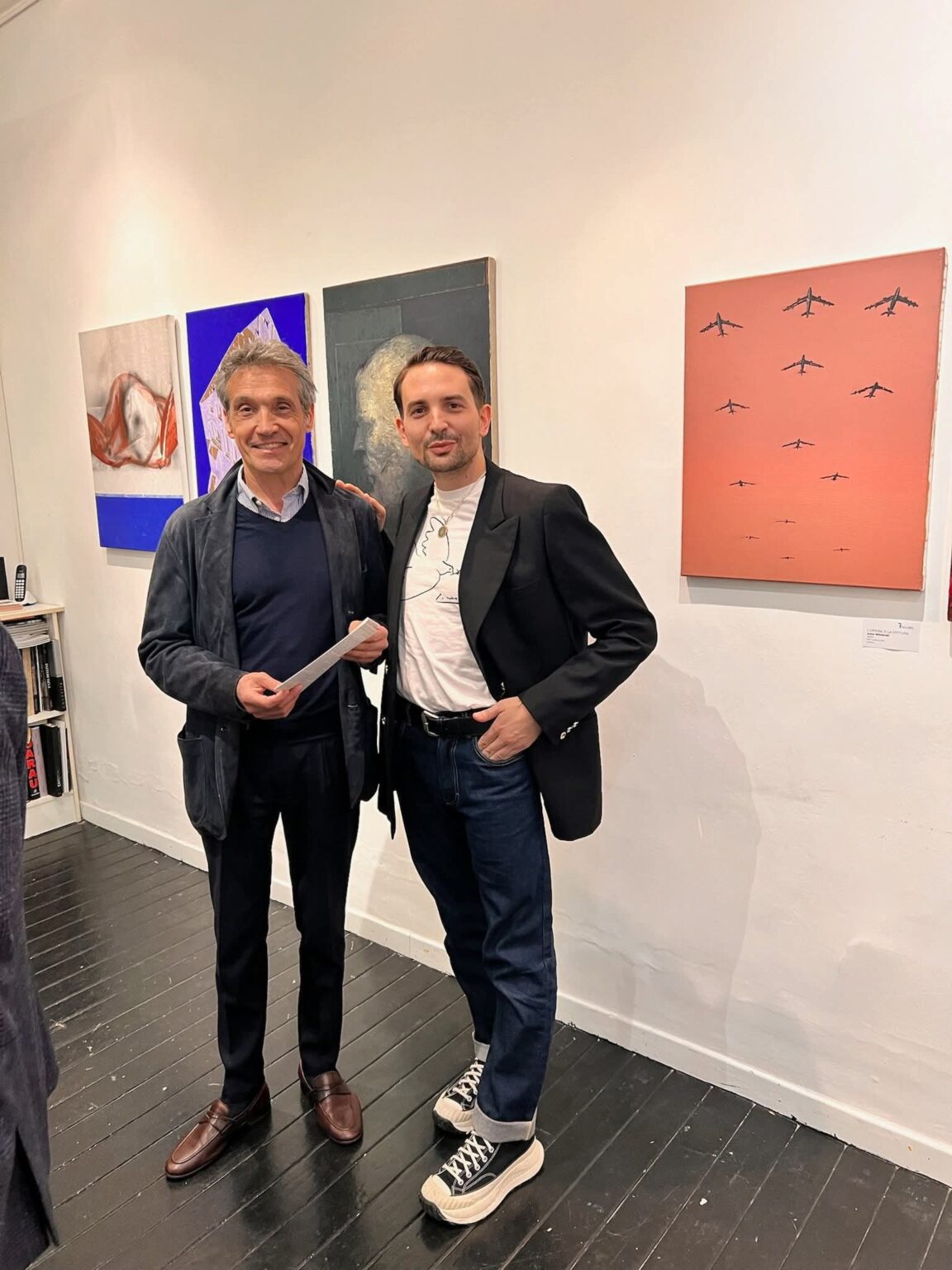 Dwie postaci stojące na tle obrazów w galerii w Rzymie.