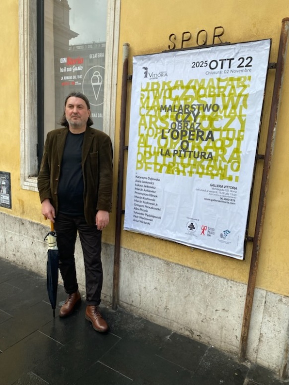 Marcin Jurkiewicz przy plakacie reklamującym wystawę.