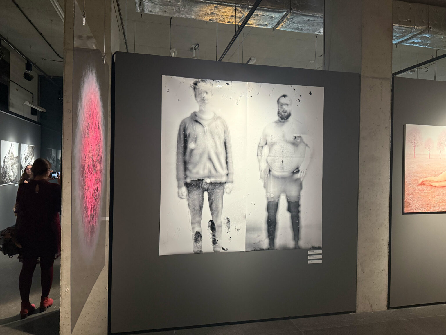 Widok dwóch fotografii mężczyzn na szarej ścianie podczas wystawy.