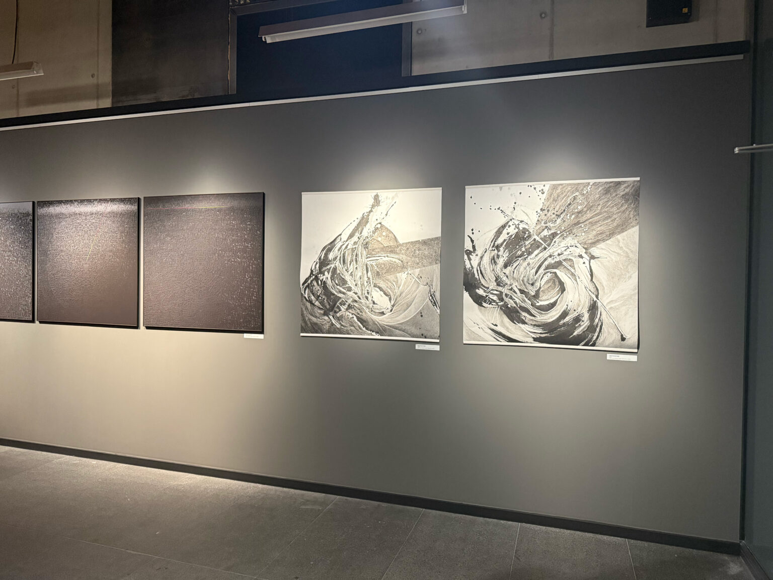 Widok wystawy z czterema pracami na szarej ścianie galerii