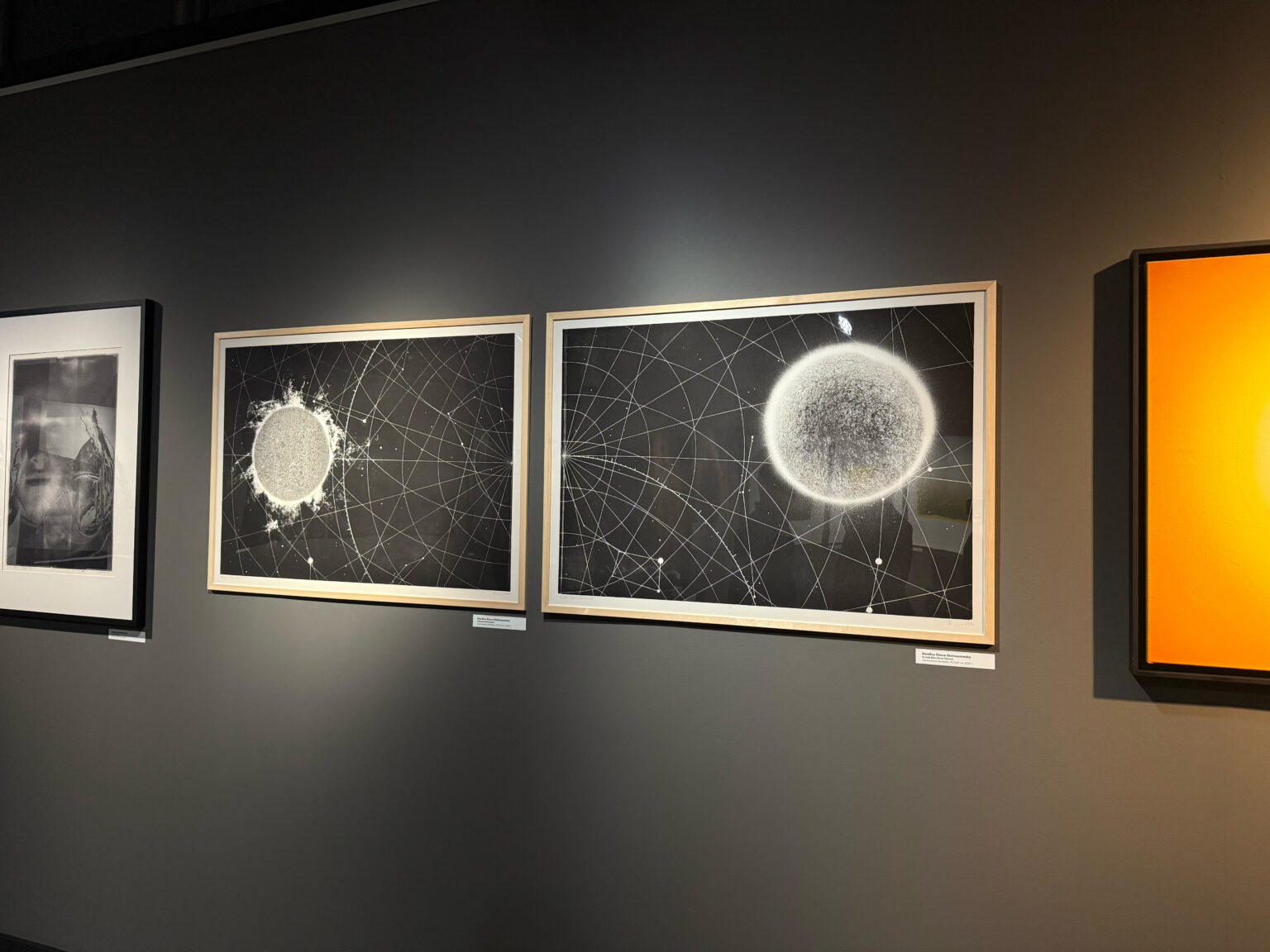 Widok dwóch grafik z Układem Słonecznym prezentowanych na szarej ścianie w galerii.