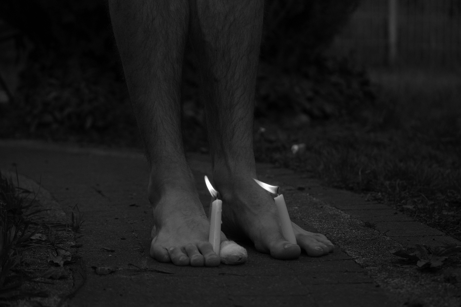 Fotografia przedstawiająca kadr stóp, ze świecami wetkniętymi między palce